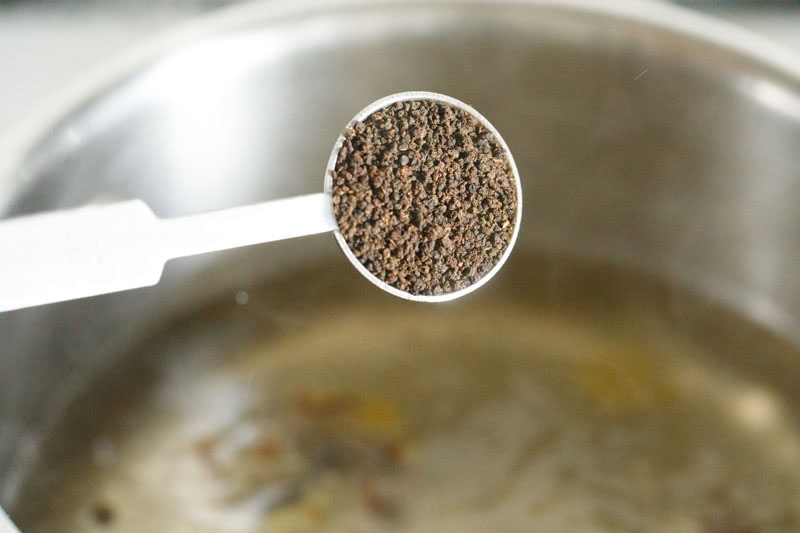 adding black tea powder to boiling water to make sulaimani chai. 