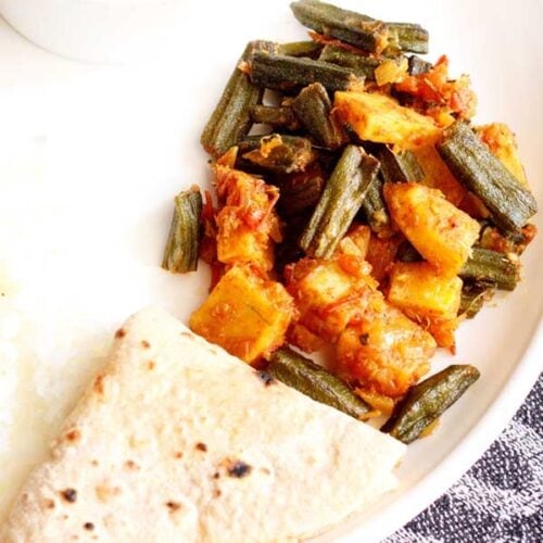 aloo bhindi served on a white plate with a folded roti.