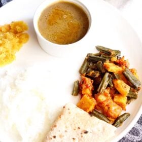 aloo bhindi served on a white plate with roti, steamed rice and dal.