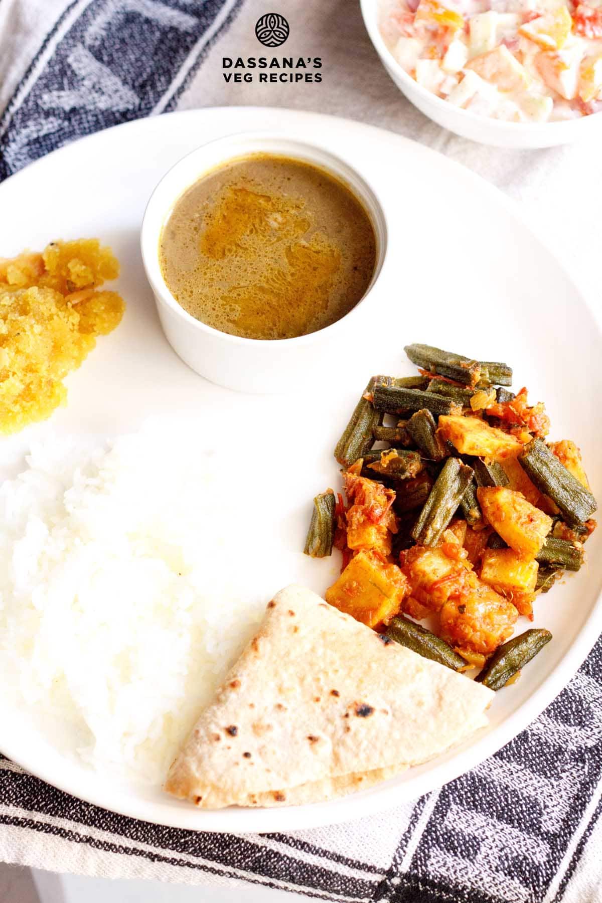 aloo bhindi served on a white plate with roti, steamed rice and dal.