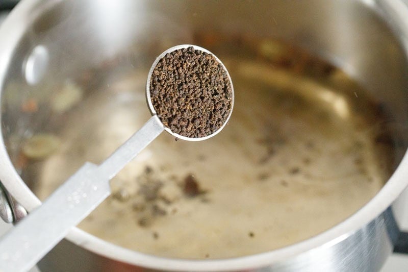 adding black tea to boiling spiced water. 