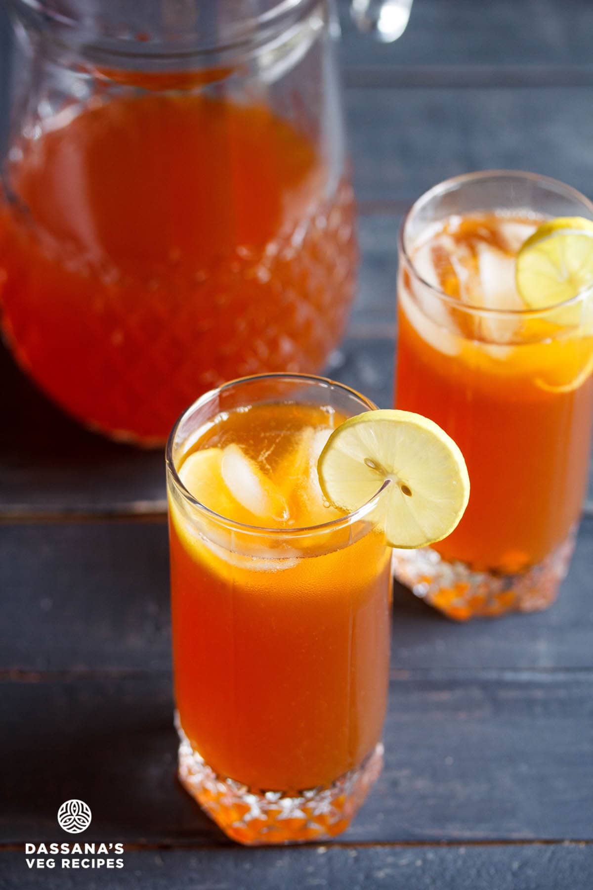 iced tea with lemon, ice cubes in two glasses with a glass pitcher full of the tea kept behind.