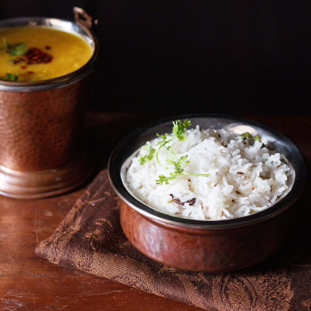 jeera rice in a small copper pan (degchi) with a small bucket of dal tadka kept behind.