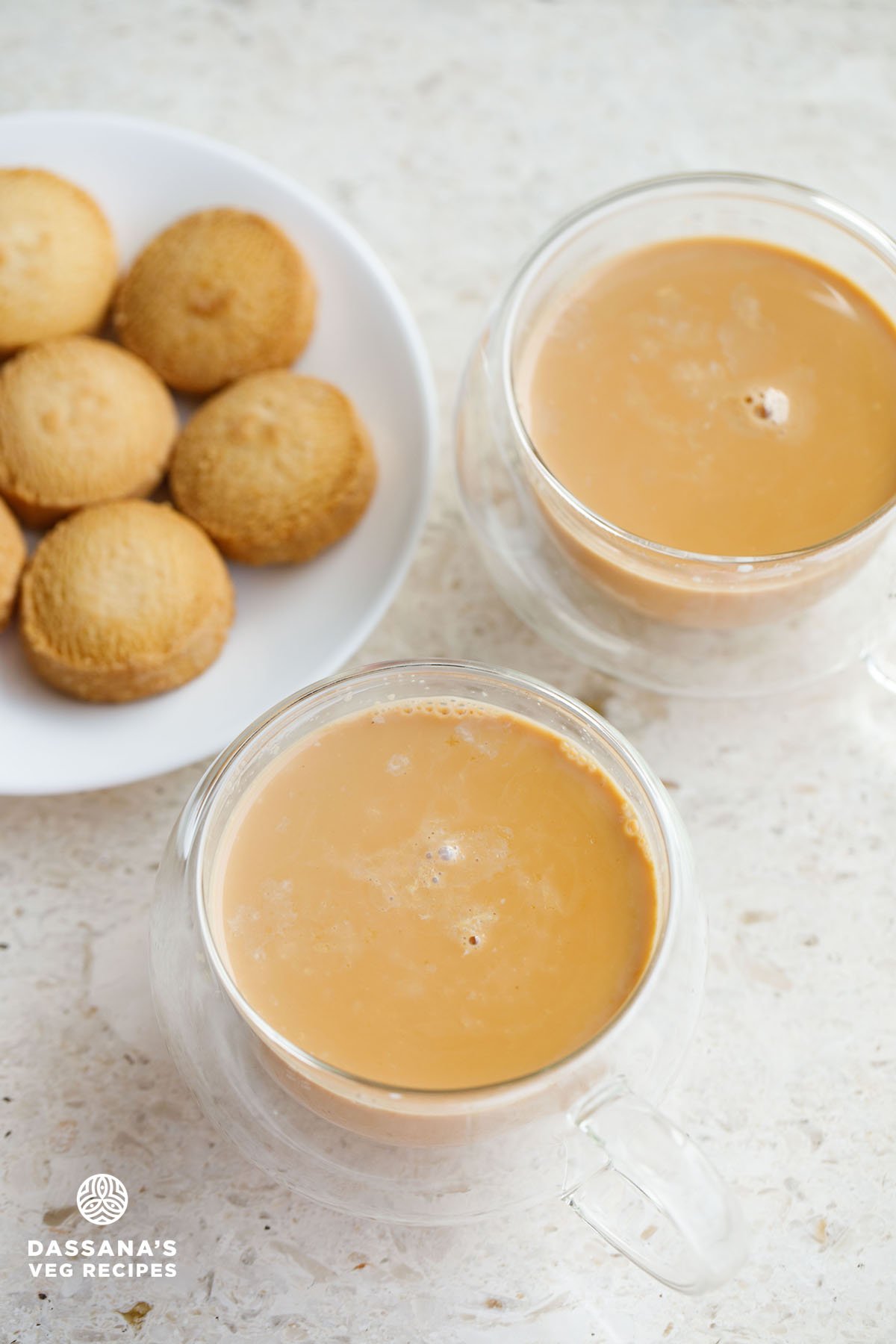 irani chai in round glass cups with a plate of osmania biscuits at the left side on a white marble background.