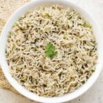 jeera rice or Indian cumin rice in a white bowl with a coriander sprig in the center.