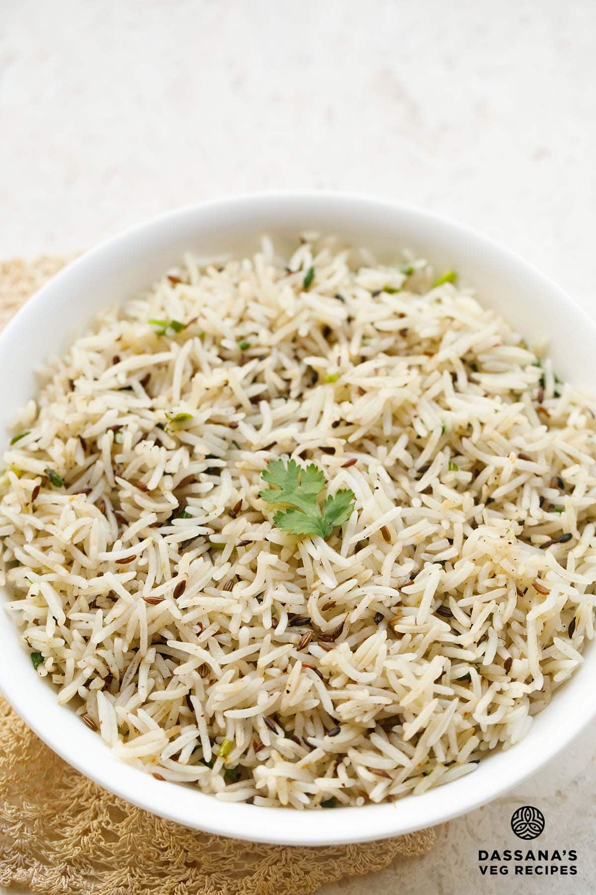 jeera rice in a white bowl with a coriander sprig in the center.