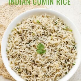 jeera rice in a white bowl with a coriander sprig in the center placed under a beige colored crocheted doily with text layovers.