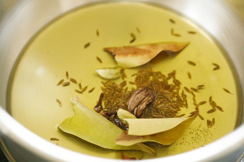 frying whole spices in hot ghee in a pan. 