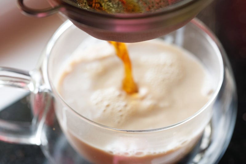 straining hot tea decoction into the cup with thickened milk. 