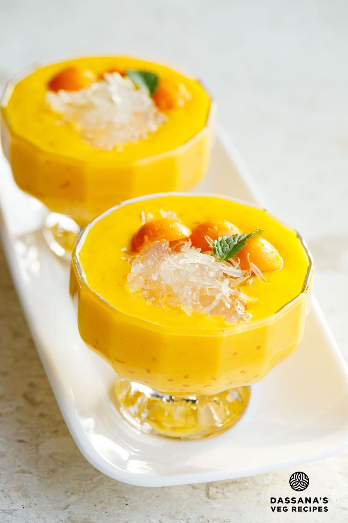 mango sago topped with sago, pomelo and a mint leaf in two glass cups with stems.