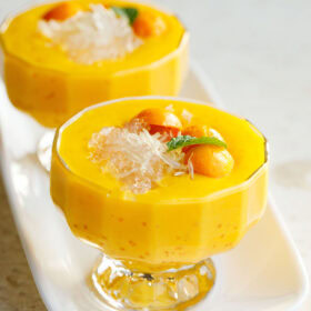 mango sago topped with sago, pomelo, mango balls, and a mint leaf in two glass cups with stems.
