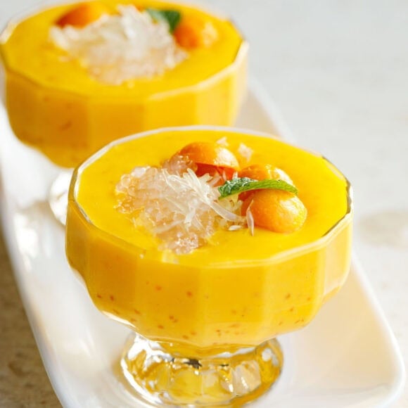 mango sago topped with sago, pomelo, mango balls, and a mint leaf in two glass cups with stems.