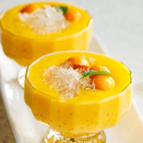 mango sago topped with sago, pomelo, mango balls, and a mint leaf in two glass cups with stems with text layovers.