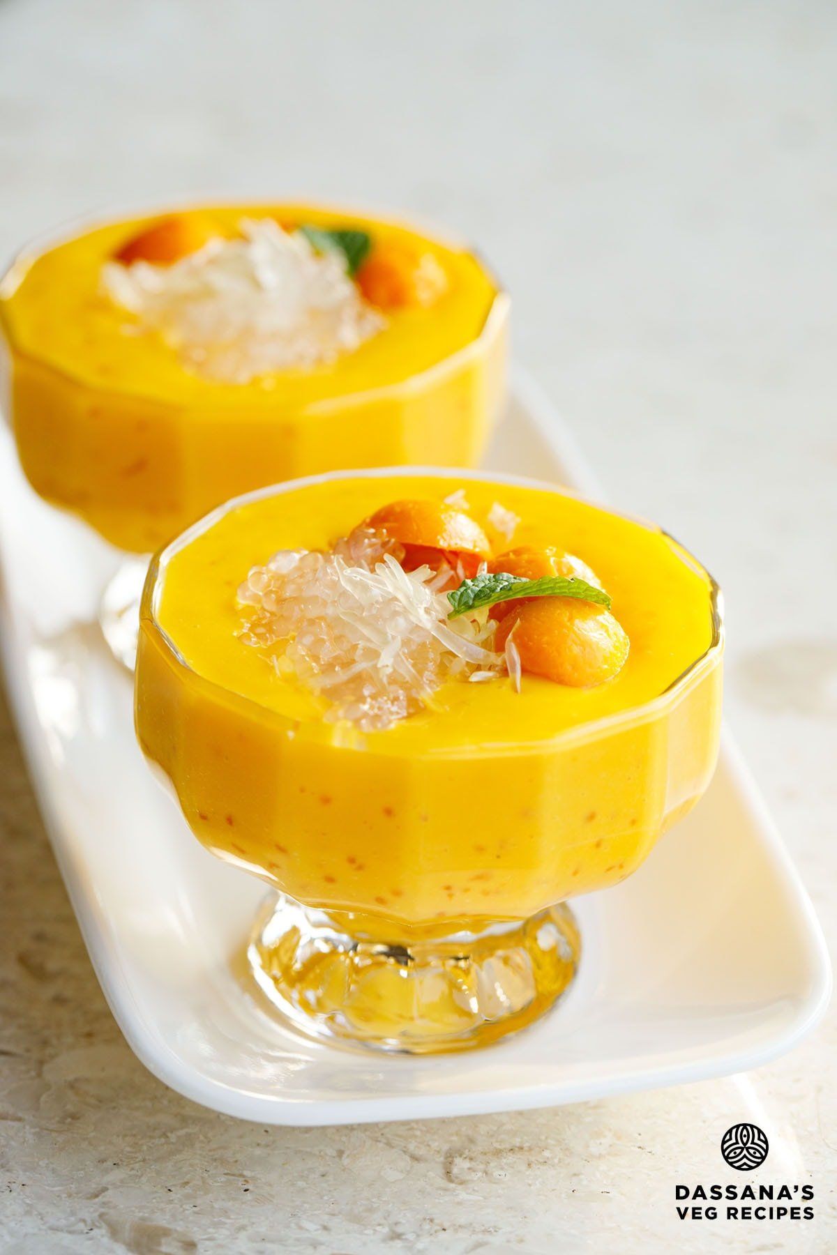 mango sago topped with sago, pomelo, mango balls, and a mint leaf in two glass cups with stems.