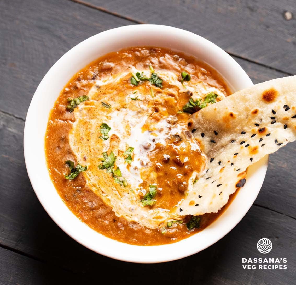 naan bread dipped in dal makhani in a white bowl.