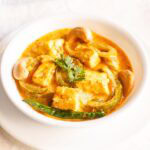 paneer sabji with coriander sprig in the center in a white bowl on a white plate.