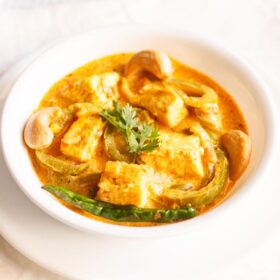paneer sabji with coriander sprig in the center in a white bowl on a white plate.