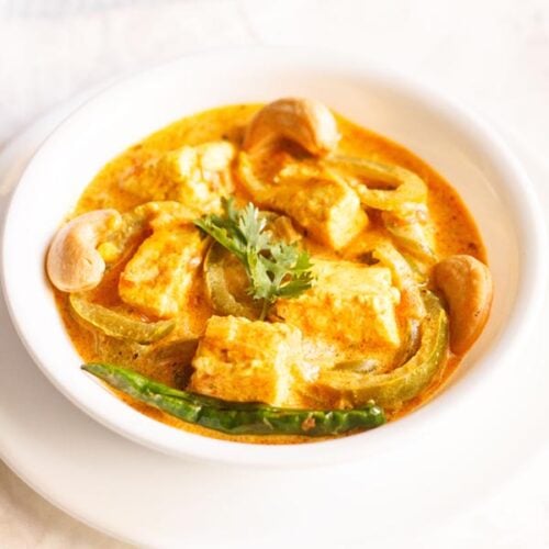 paneer sabji with coriander sprig in the center in a white bowl on a white plate.