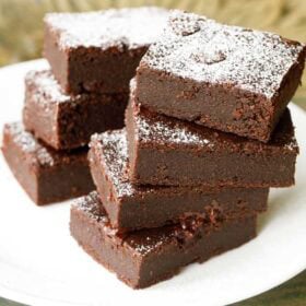 brownie sprinkled with powdered sugar, cut into squares, stacked on top of each other on a white plate.