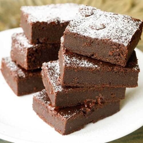 brownie sprinkled with powdered sugar, cut into squares, stacked on top of each other on a white plate.