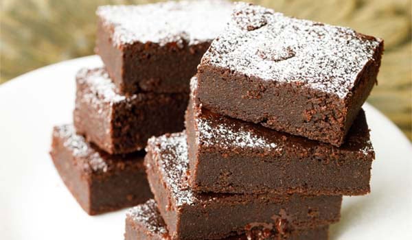 close up image of brownie sprinkled with powdered sugar, cut into rectangles, stacked on top of each other.