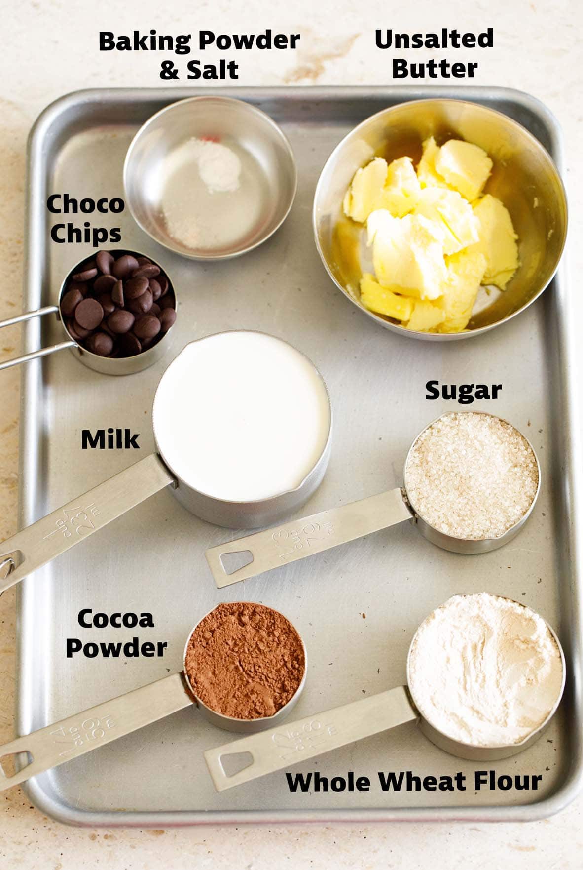 eggless brownie ingredients in measuring cups and bowls placed on a tray.