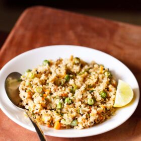oats upma with lemon wedge and a spoon on white plate on a brown board.