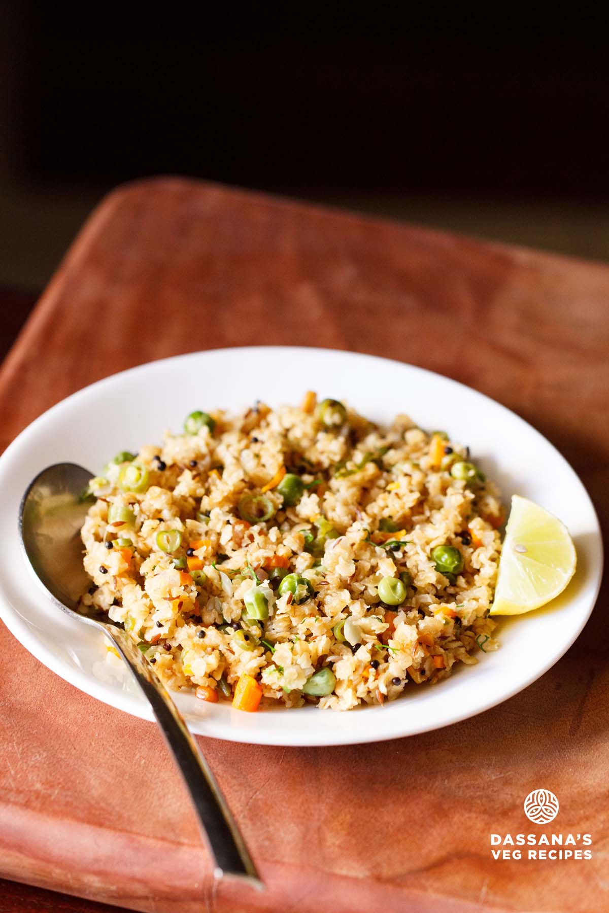 oats upma with lemon wedge and a spoon on white plate on a brown board.