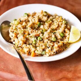 oats upma with lemon wedge and a spoon on white plate on a brown board.