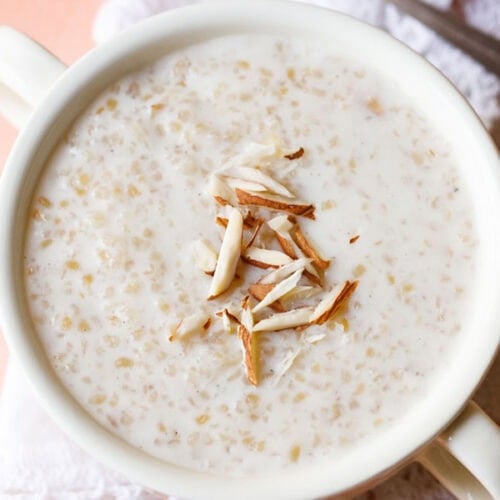wheat porridge with slivered almonds in the center in a white bowl with handles.