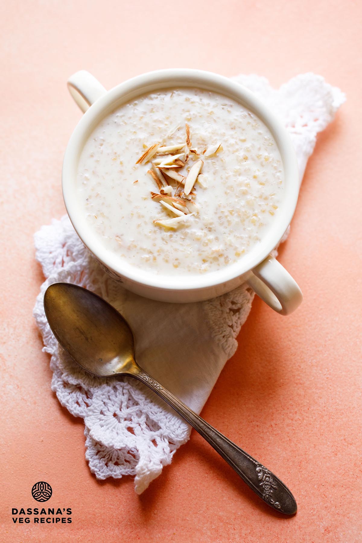 wheat porridge with slivered almonds in a white bowl with handles on a white folded doily with brass spoon below.