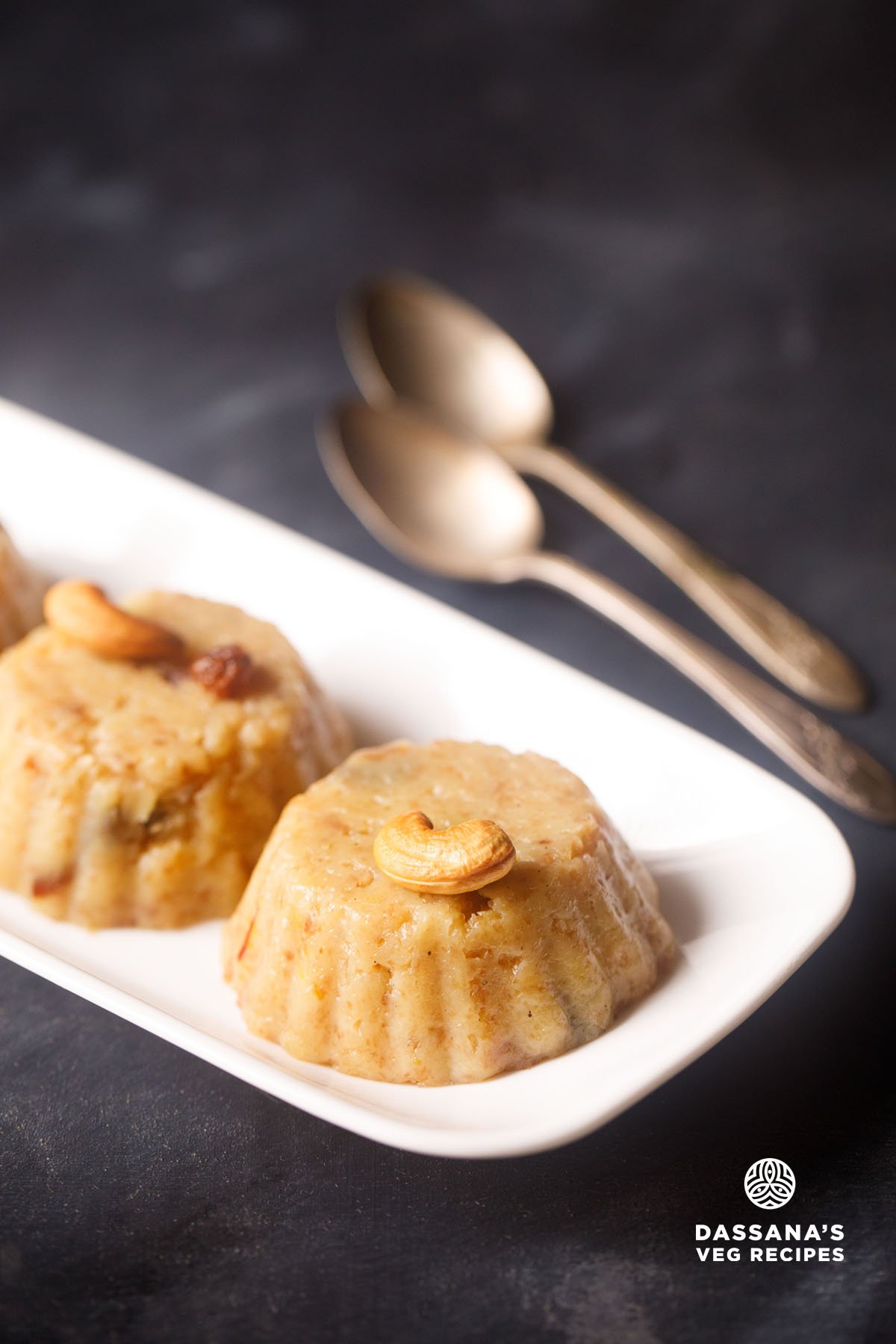 bread halwa on a white platter with two silver spoons on top.