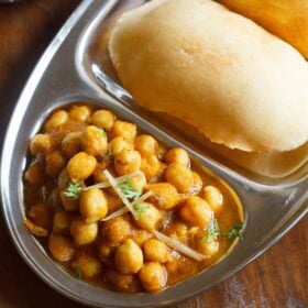 chole bhature on a plate with sections for chana curry and fried bread.
