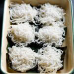 idiyappam (nool puttu) sprinkled with grated coconut and placed over banana leaves on a tray.