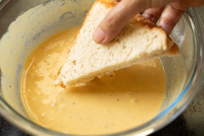 assembled bread with potato stuffing being dipped in besan batter.
