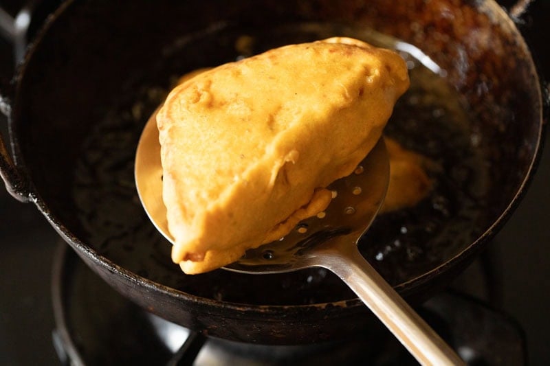 fried potato stuffed bread pakora on a slotted spoon