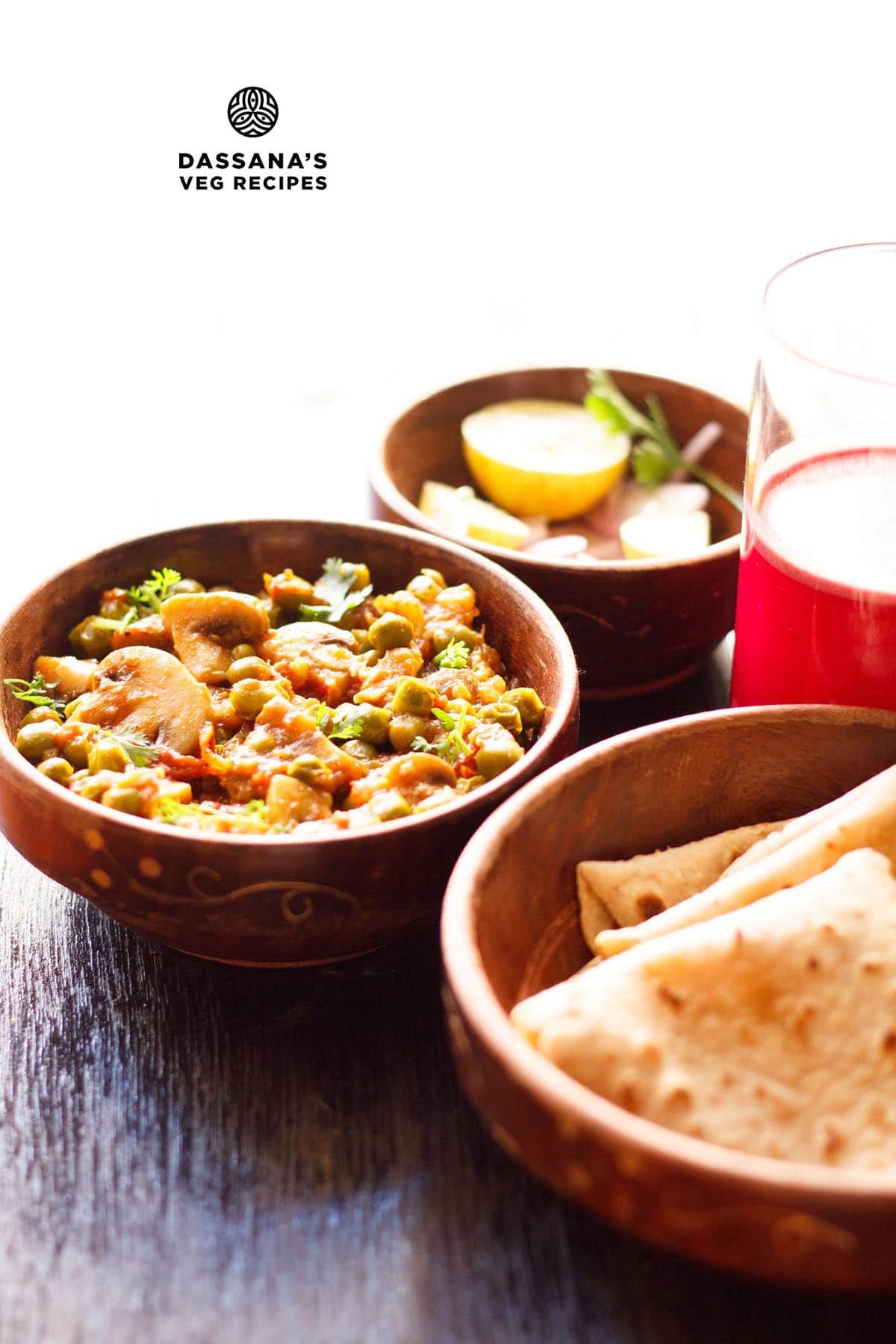 matar mushroom garnished with chopped coriander leaves and served in a wooden bowl along with a bowl of chapatis, onion and lemon and a glass of carrot kanji kept on the right side.
