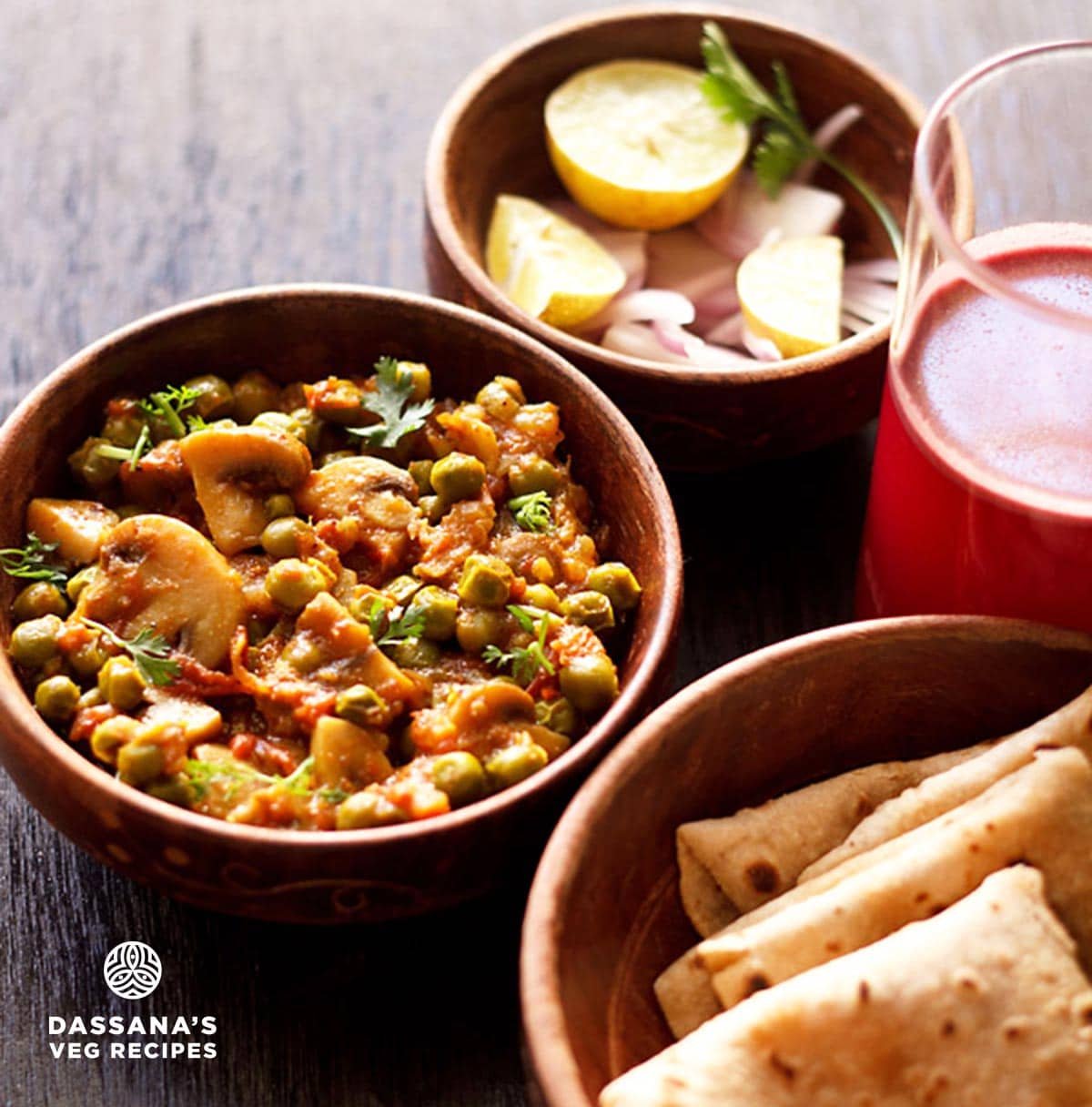 mutter mushroom garnished with chopped coriander leaves and served in a wooden bowl along with a bowl of chapatis, onion and lemon and a glass of kanji kept on the right side. 