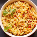 tomato rice with a coriander sprig in a bowl.