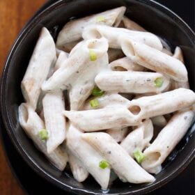 white sauce pasta garnished with scallion greens served in a black bowl.