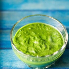 bright green colored sandwich chutney in a glass bowl on a blue wooden tray.