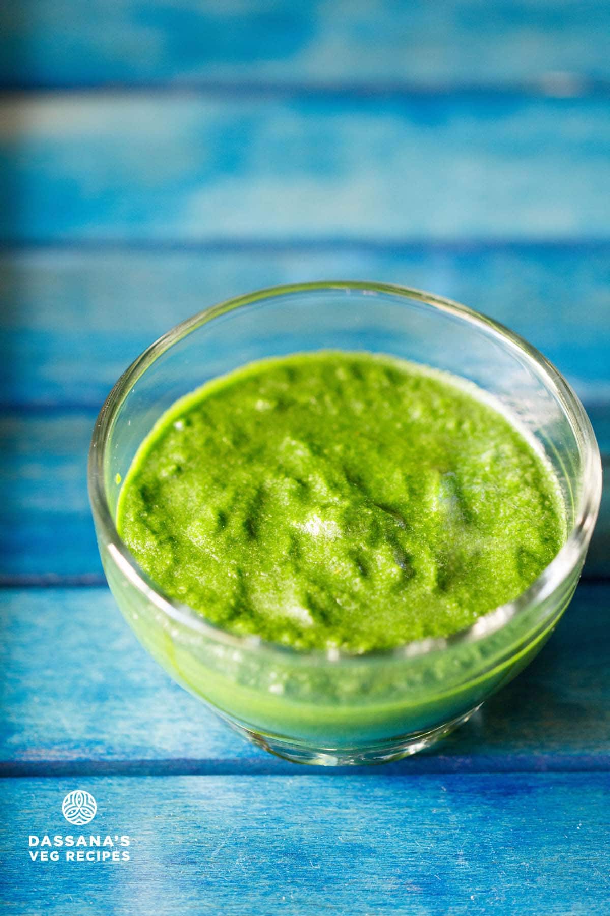 bright green colored sandwich chutney in a glass bowl on a blue wooden tray.