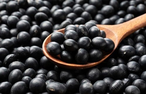 closeup image of black soybeans in a spoon placed on a bed of black soybeans.