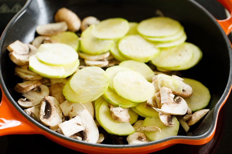 Sliced zucchini and mushrooms in skillet.