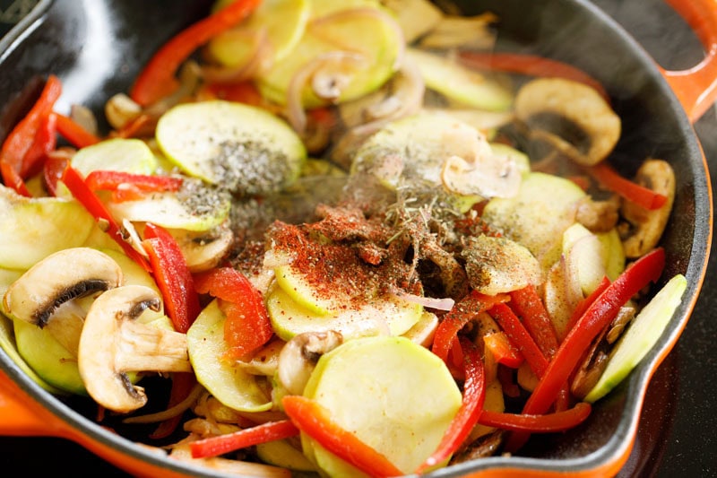 spices and herbs sprinkled on top of the sautéed vegetables in a skillet