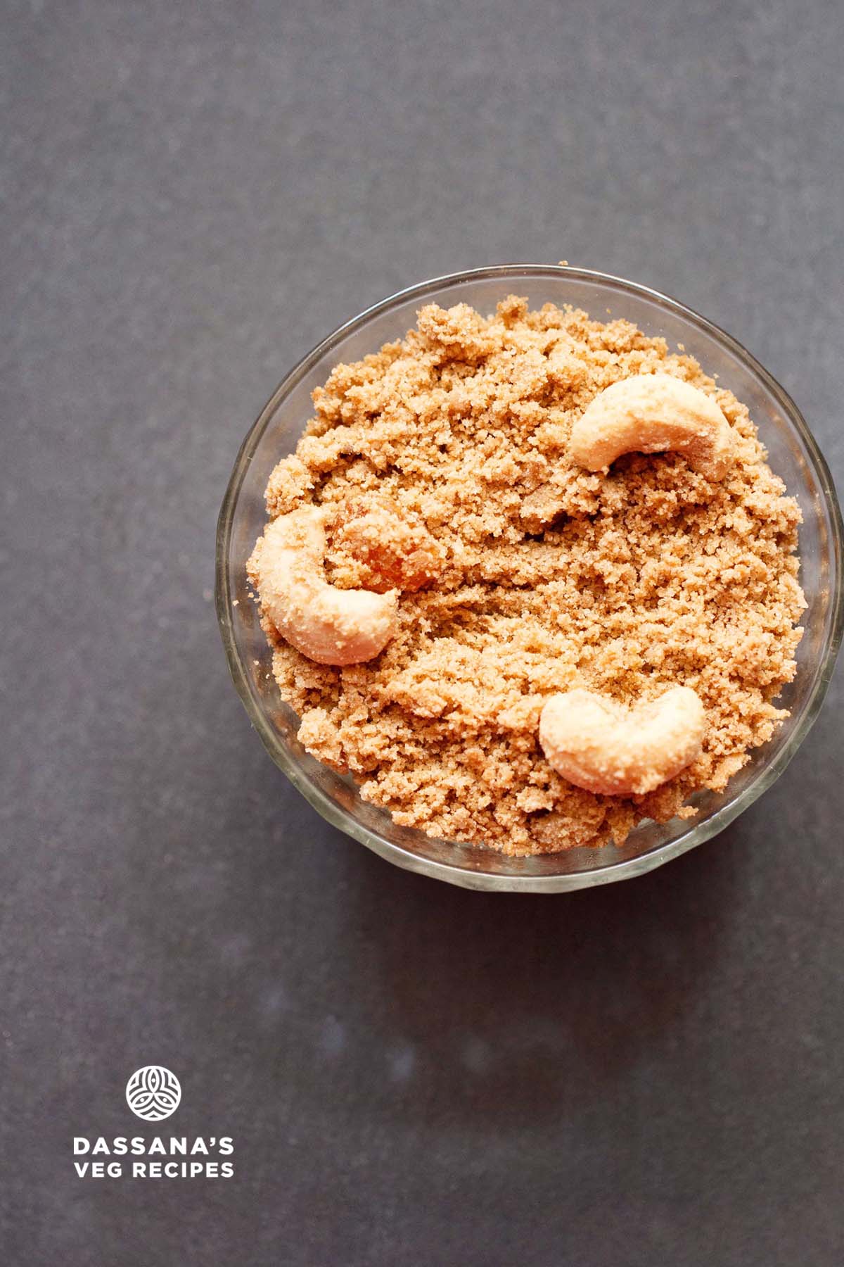 panjiri in a glass bowl topped with cashews on a dark grey table.
