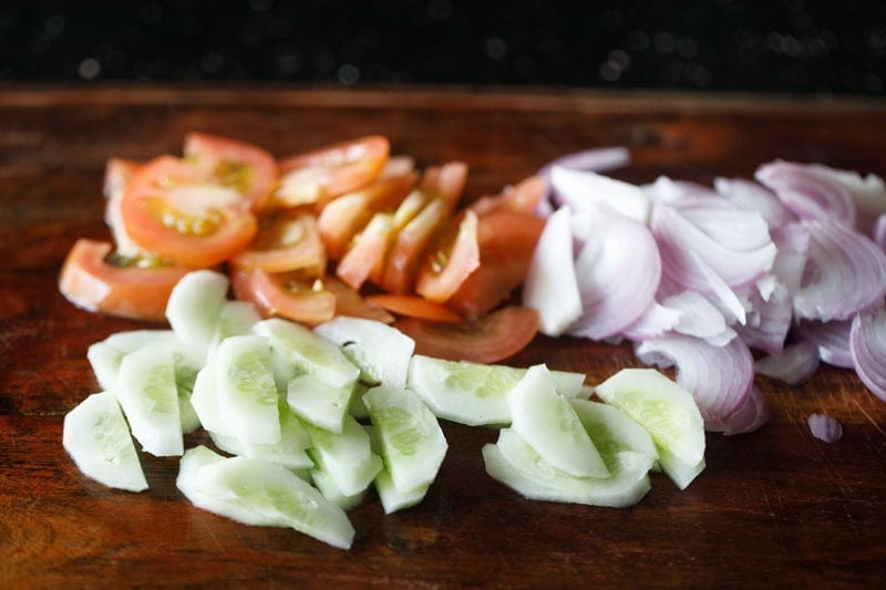 thinly sliced onions, tomatoes, cucumbers on chopping board.