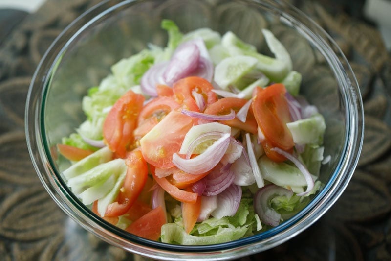 sliced onions, cucumber, tomatoes added on top of lettuce in mixing bowl.