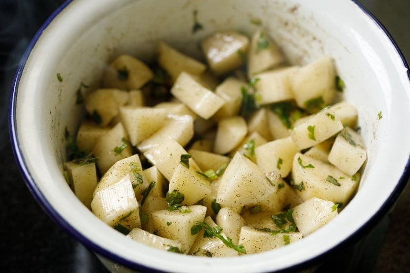 Chopped potatoes evenly mixed with herbs and oils in a bowl.