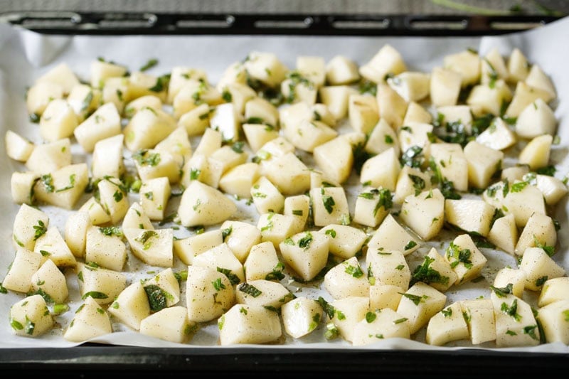 Chopped potatoes seasoned with herbs on a parchment lined baking tray.
